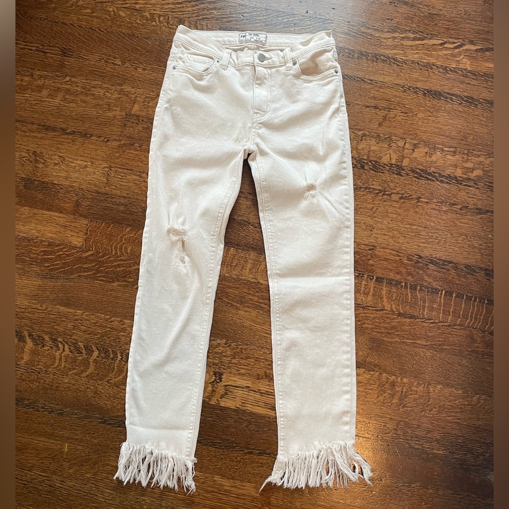 cream colored free people jeans with rips and fringe accents